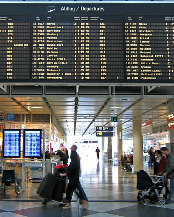 Travellers wheeling suitcases through an airport departures hall.