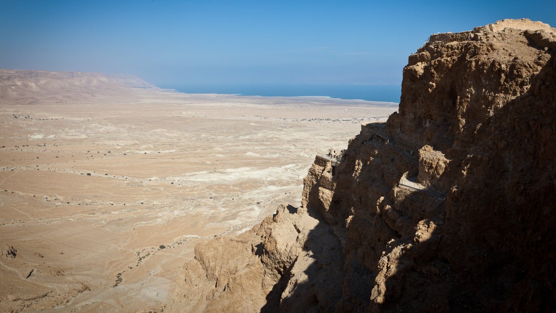 The cliffs of Masada rising above the desert plain, with the Dead Sea beyond.